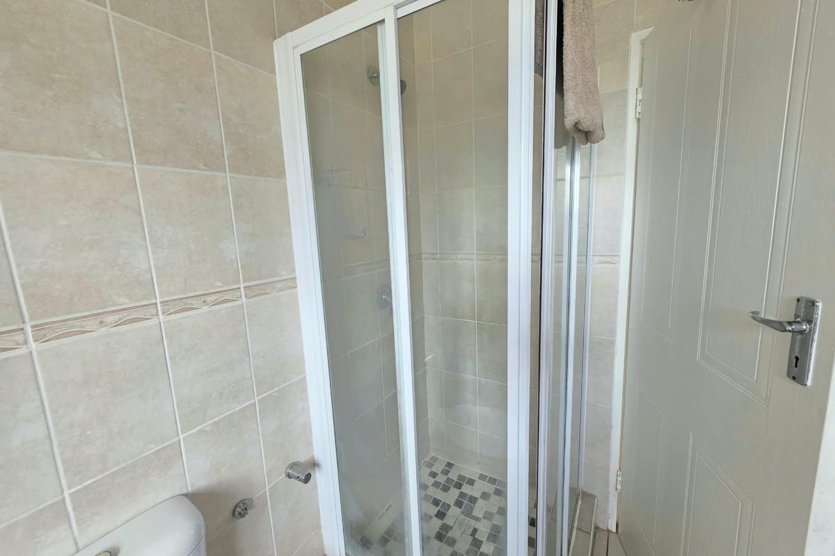 A functional bathroom featuring a corner shower enclosure with tiled walls and mosaic floor detailing, alongside a standard toilet and interior door.