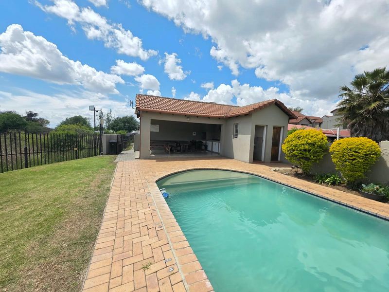 Outdoor entertainment area featuring a swimming pool, brick-paved surround, and a covered patio structure set within a landscaped garden.