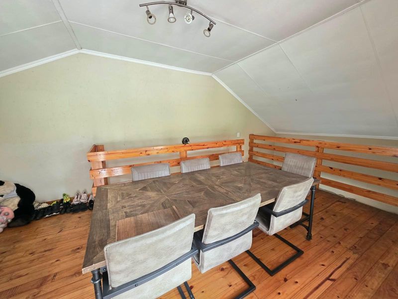A dining area featuring timber flooring, a sloped ceiling with track lighting, and a wooden balustrade overlooking the lower level.