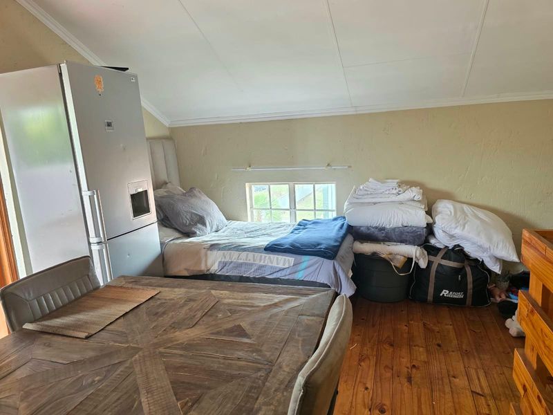 A bedroom space featuring timber flooring and a pitched ceiling with a small casement window, requiring cosmetic updates to the wall finishes.