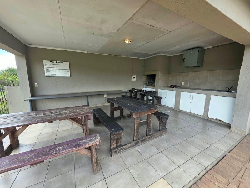 Covered outdoor patio area featuring a built-in braai, tiled flooring, and a kitchenette with sink and storage cabinetry.