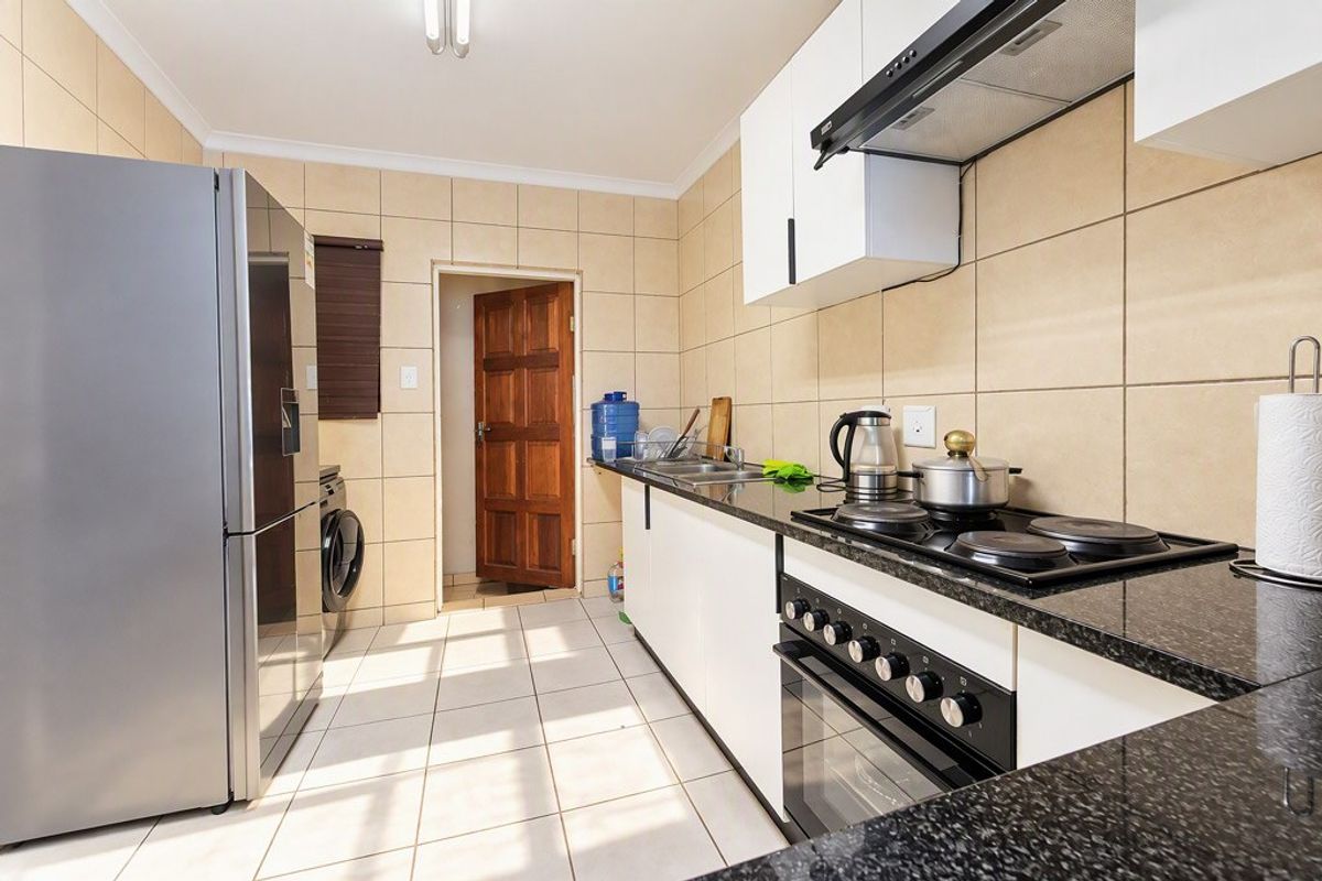 A functional kitchen featuring granite countertops, built-in cabinetry, an electric hob with extractor fan, and tiled finishes throughout.