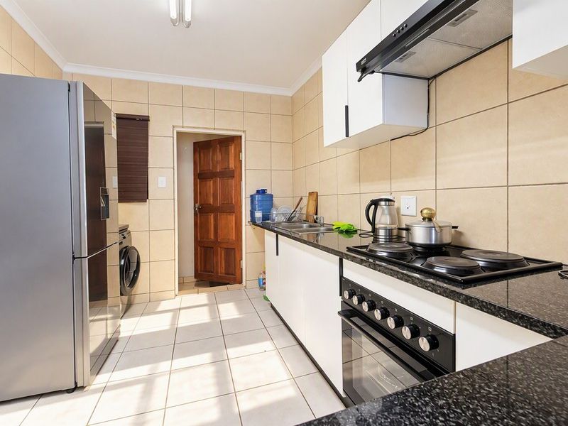 A functional kitchen featuring granite countertops, built-in cabinetry, an electric hob with extractor fan, and tiled finishes throughout.