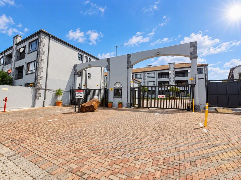 The secure entrance to the apartment complex features a paved driveway, gated access, and a decorative architectural archway.