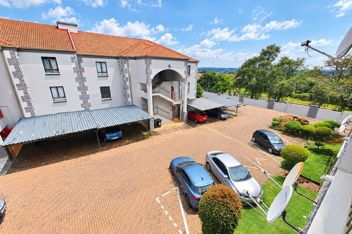 Elevated view of the apartment complex exterior, featuring paved parking areas, covered carports, and landscaped garden surroundings.