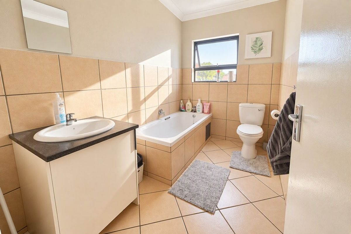 A functional bathroom featuring a built-in vanity with basin, a tiled bathtub, and a standard toilet, finished with neutral wall and floor tiles.