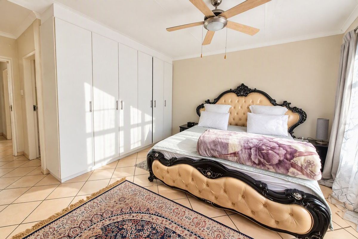 A well-maintained bedroom featuring built-in cupboards, a ceiling fan, and neutral tiled flooring, offering a clean and functional living space.
