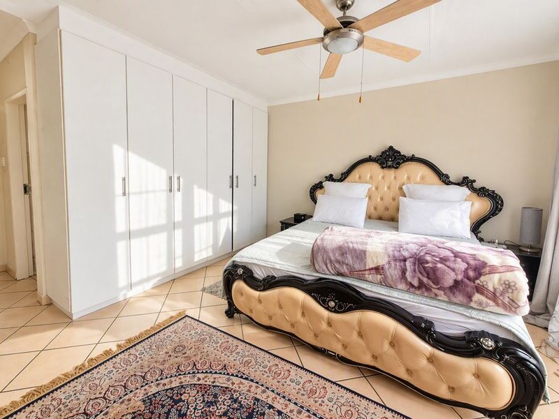 A well-maintained bedroom featuring built-in cupboards, a ceiling fan, and neutral tiled flooring, offering a clean and functional living space.