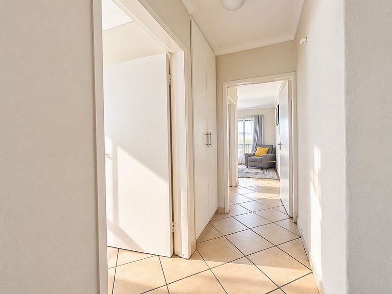 A bright and clean hallway featuring neutral tiled flooring and built-in storage cupboards, providing access to adjacent rooms.