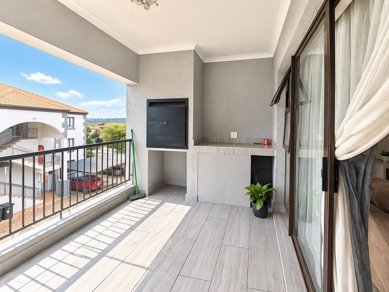 A spacious covered balcony featuring a built-in braai, stone countertop, and modern tiled flooring, offering an ideal space for outdoor entertaining.