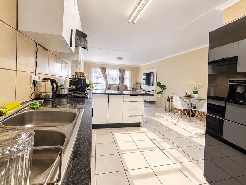 Open-plan kitchen and living area featuring modern cabinetry, granite countertops, integrated appliances, and tiled flooring throughout.