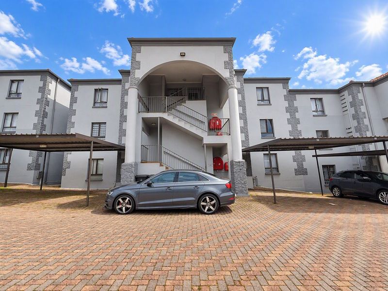 Front view of an apartment complex featuring a paved parking area with carports and an external staircase leading to upper levels.