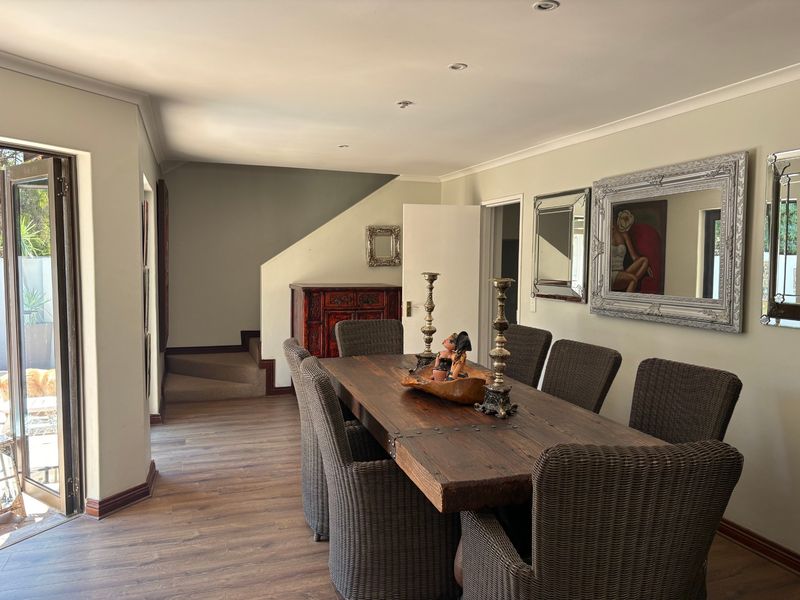 A well-lit dining room featuring laminate flooring, recessed downlights, and direct access to an outdoor area via glass doors.