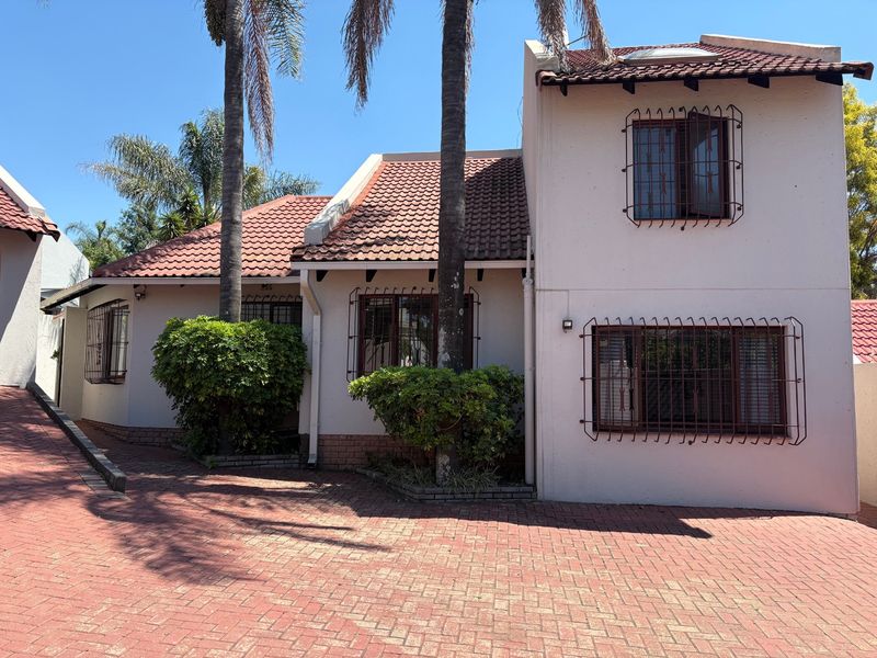 Front elevation of a cluster home featuring a terracotta tiled roof, paved driveway, and security bars on windows.