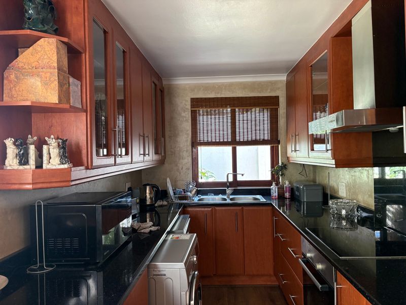 A functional kitchen featuring cherry wood cabinetry, black granite countertops, a stainless steel extractor fan, and a built-in oven with a double sink.