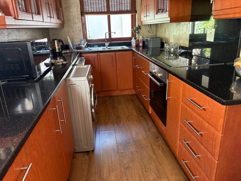 A functional kitchen featuring warm-toned wooden cabinetry, black granite countertops, integrated oven and hob, and durable laminate flooring.