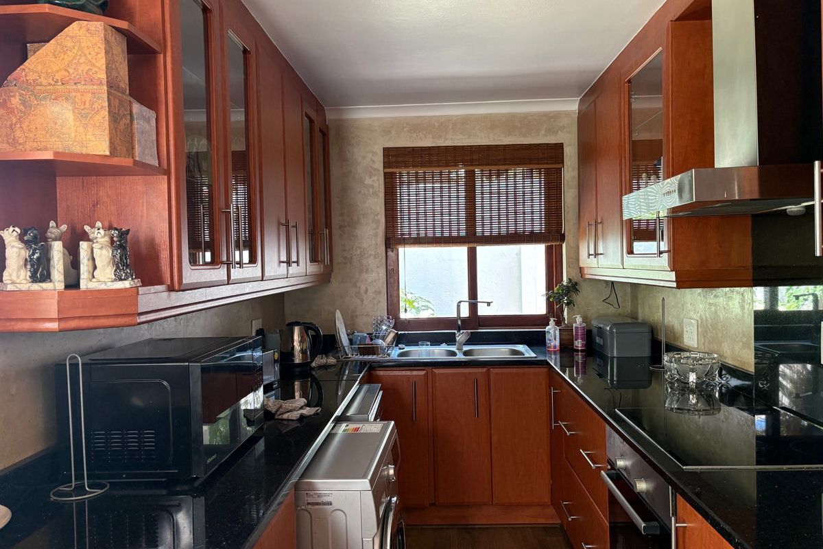 A functional kitchen featuring cherry wood cabinetry, black granite countertops, a stainless steel double sink, and integrated appliances including an oven and extractor fan.