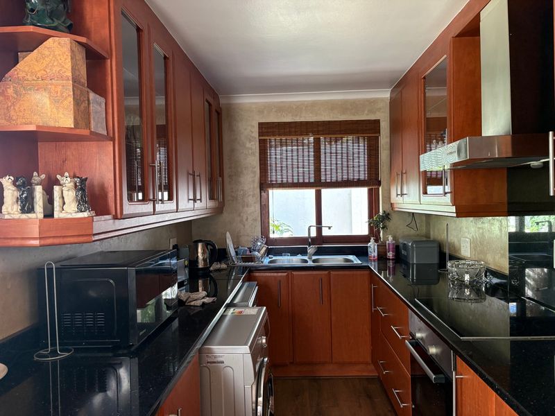 A functional kitchen featuring cherry wood cabinetry, black granite countertops, a stainless steel double sink, and integrated appliances including an oven and extractor fan.