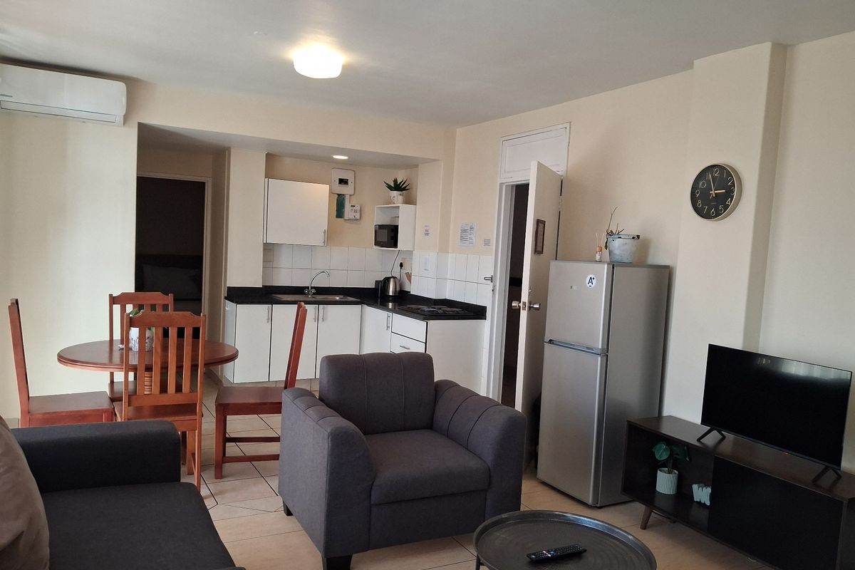 Open-plan living and kitchen area featuring tiled flooring, built-in cabinetry with laminate countertops, and a wall-mounted air conditioning unit.