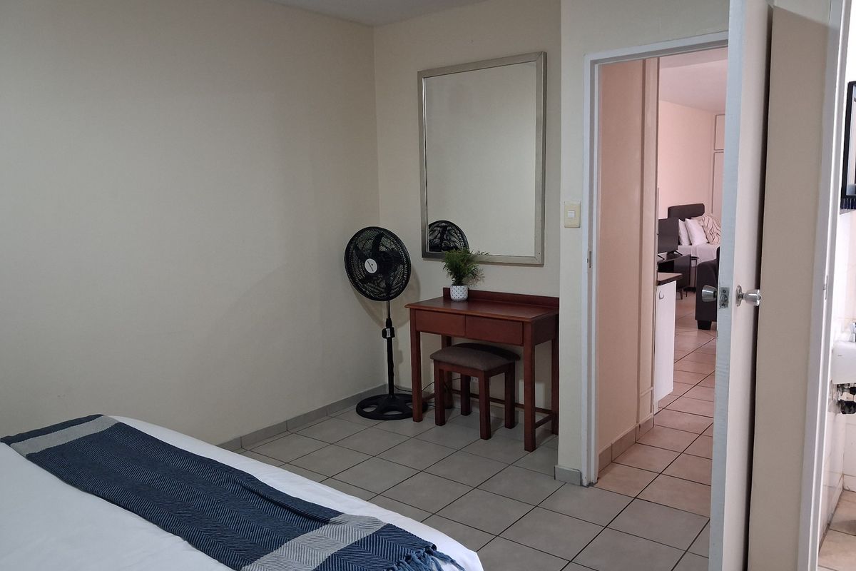 A bedroom featuring tiled flooring and a doorway leading to an adjacent living area, providing a functional and connected layout.