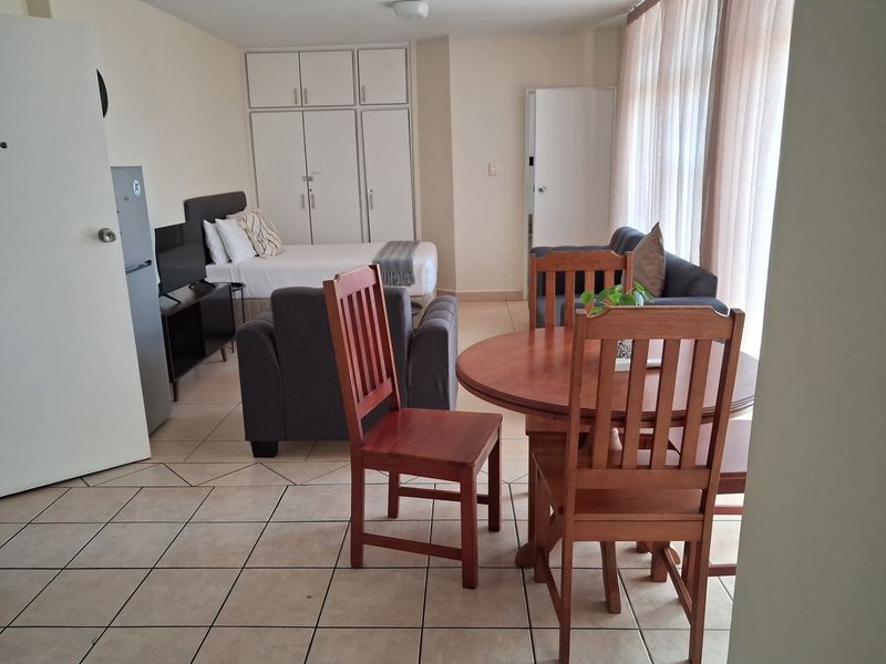 Open-plan studio apartment featuring tiled flooring, built-in cupboards, and large windows allowing for natural light.