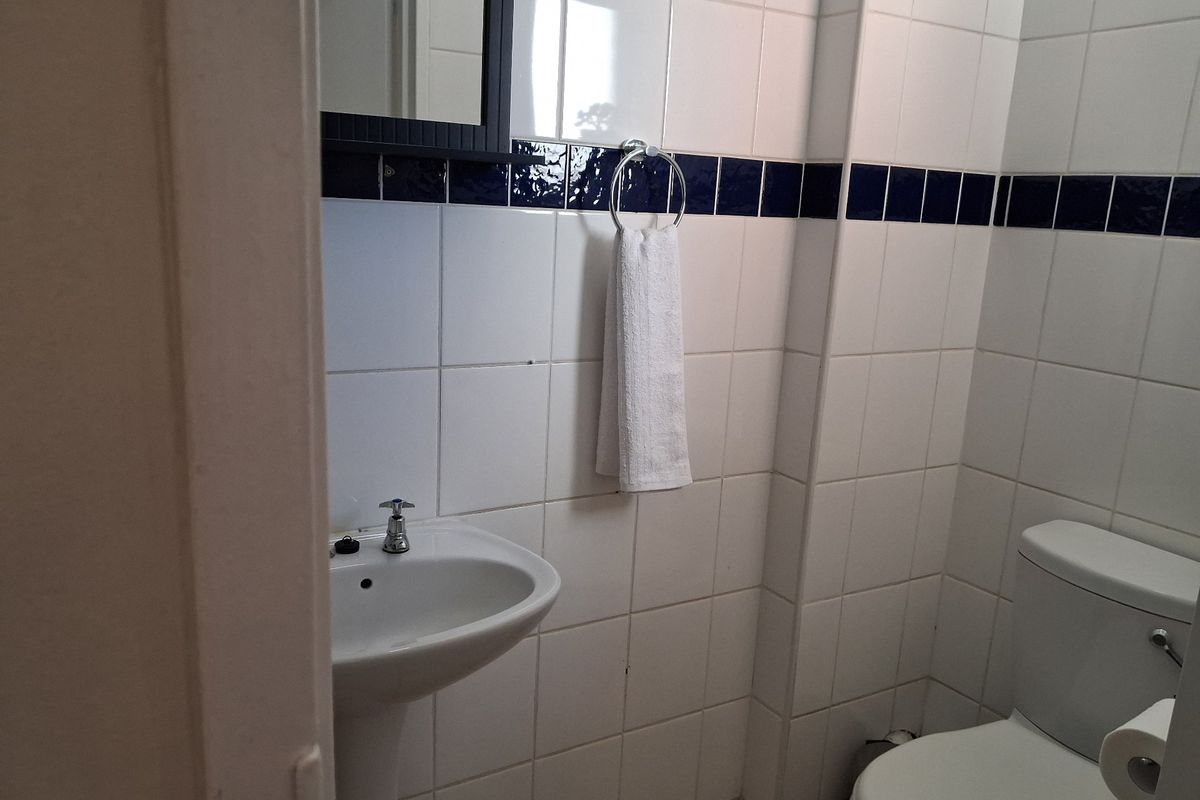A compact bathroom featuring a pedestal basin, toilet, and classic white wall tiling with a decorative blue accent border.