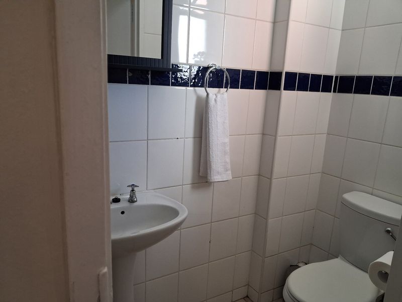 A compact bathroom featuring a pedestal basin, toilet, and classic white wall tiling with a decorative blue accent border.