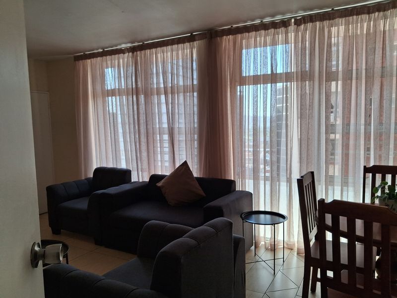 An open-plan living and dining area featuring large floor-to-ceiling windows that provide ample natural light and a view of the surrounding urban environment.