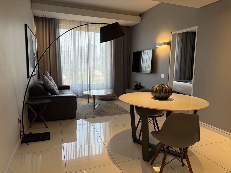 A modern open-plan living and dining area featuring polished tiled floors, recessed ceiling lighting, and a sliding glass door leading to a balcony.