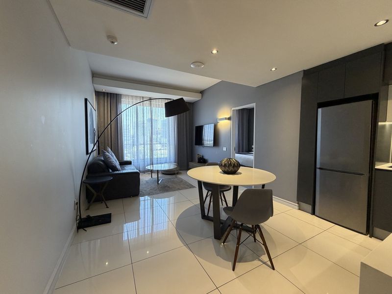 Modern open-plan living and dining area featuring glossy tiled flooring, recessed lighting, and integrated kitchen cabinetry in a contemporary apartment setting.