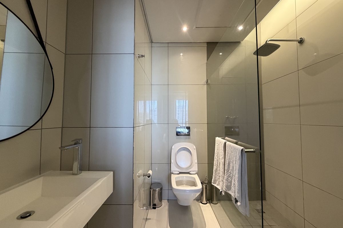 Modern bathroom featuring a wall-mounted toilet, glass-enclosed rain shower, and a sleek wall-mounted basin with contemporary chrome fixtures and neutral tiling.