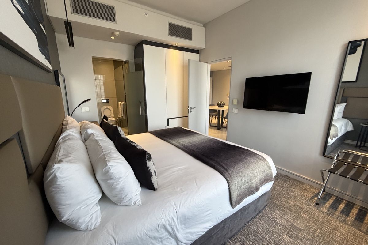 A modern bedroom featuring a built-in wardrobe, central air conditioning, and an en-suite bathroom, finished with neutral tones and carpeted flooring.