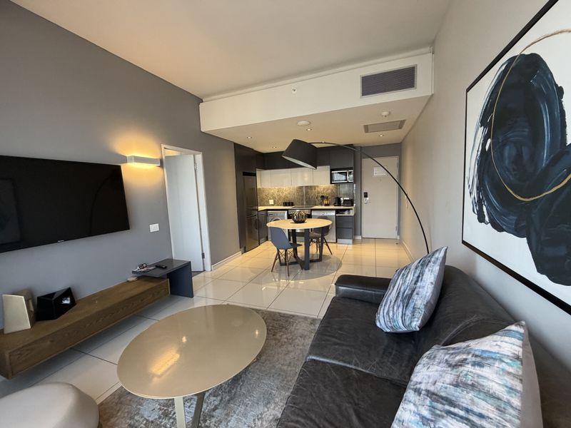 Modern open-plan apartment featuring a sleek kitchen with built-in cabinetry and stone backsplash, flowing into a comfortable living and dining area with tiled floors.