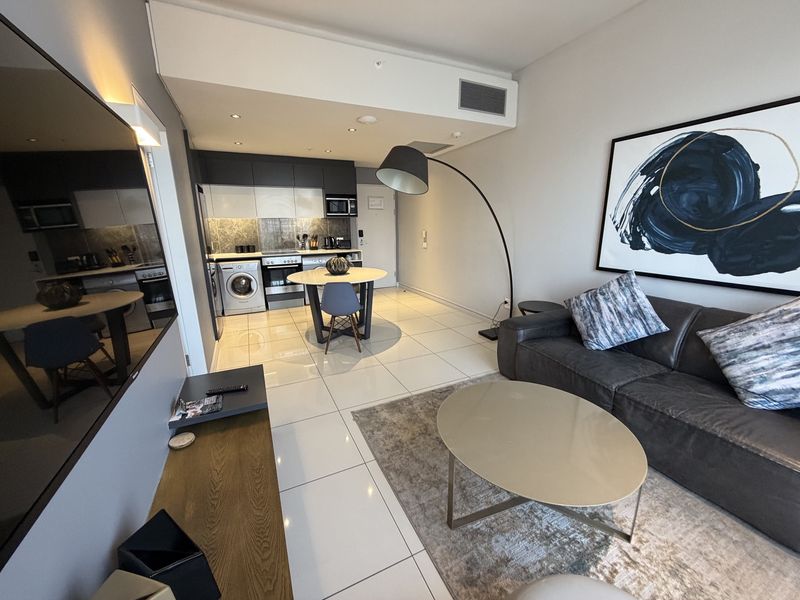 Modern open-plan apartment featuring a sleek kitchen with integrated appliances, tiled flooring, and a seamless transition into the living area.