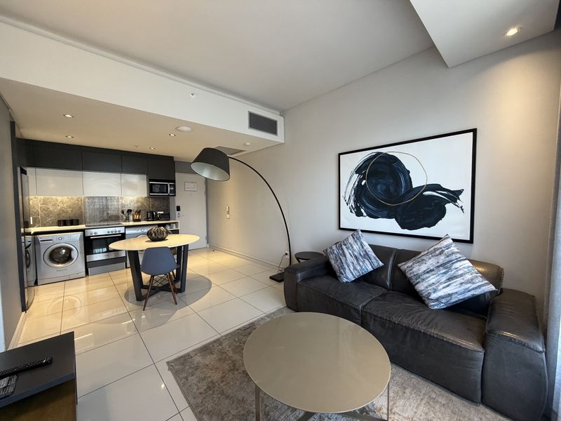A modern open-plan apartment featuring a sleek kitchen with built-in appliances and a comfortable living area with tiled flooring and recessed lighting.