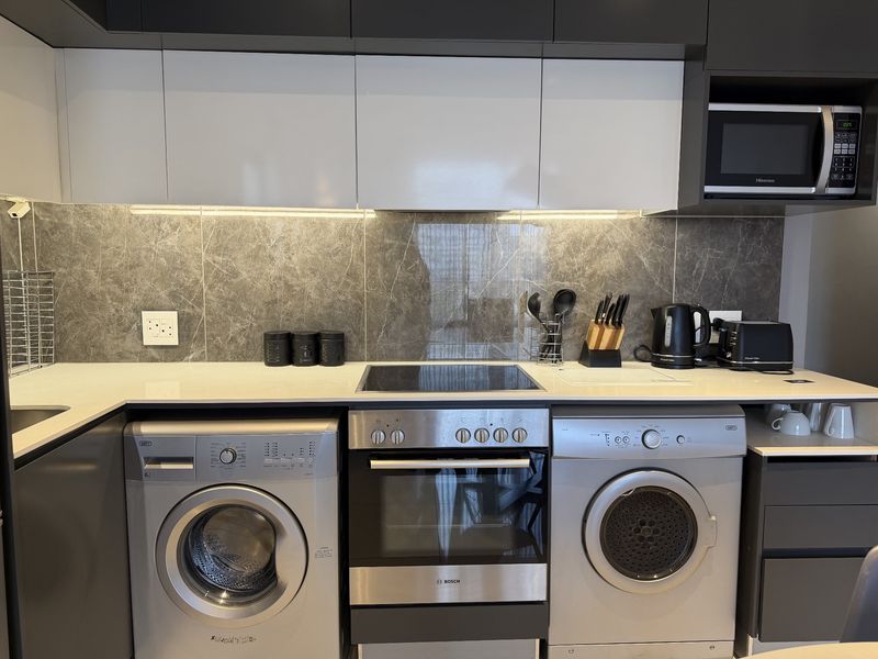 Modern kitchen featuring sleek two-tone cabinetry, stone countertops, marble-look splashback, and integrated appliances including an oven, hob, and microwave.