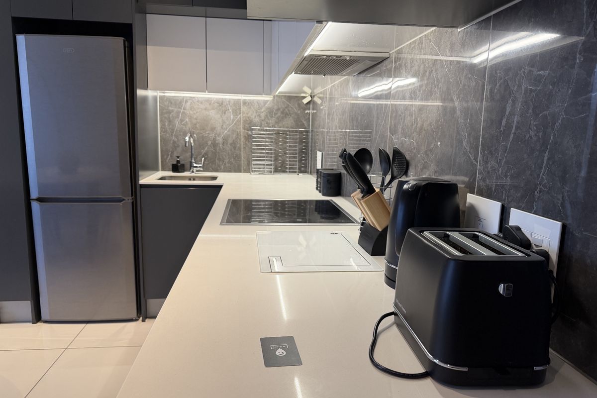 Modern kitchen featuring sleek dark cabinetry, stone countertops, marble-look splashback, and integrated appliances including an induction hob and extractor fan.