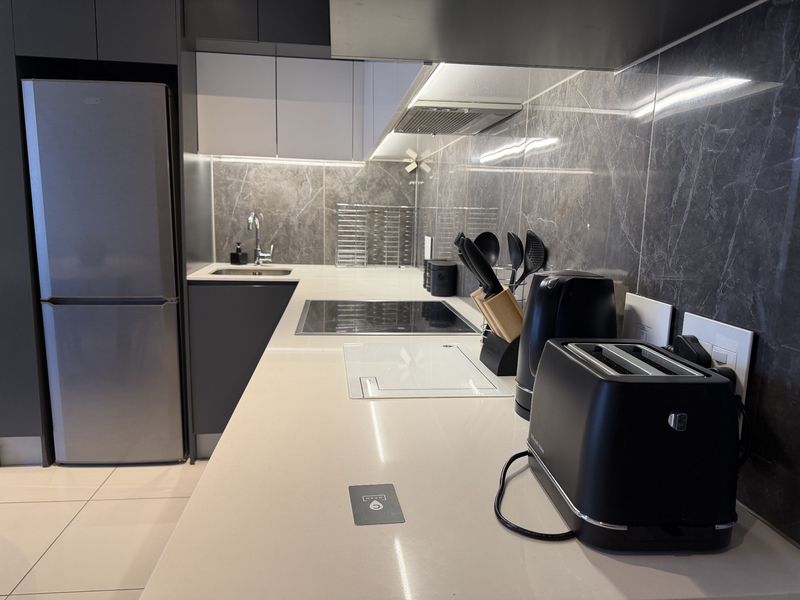 Modern kitchen featuring sleek dark cabinetry, stone countertops, marble-look splashback, and integrated appliances including an induction hob and extractor fan.
