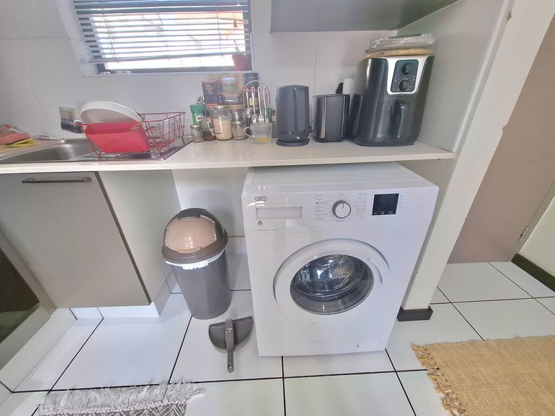 A functional laundry area featuring built-in cabinetry, a stainless steel sink, and tiled flooring, providing a practical space for household chores.