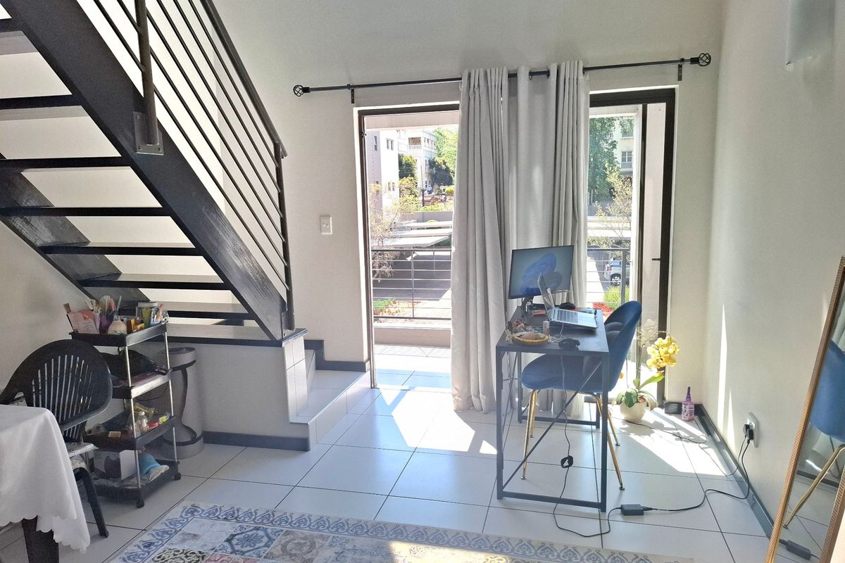 A bright living area featuring tiled flooring, a modern metal staircase, and direct access to a balcony through a sliding glass door.