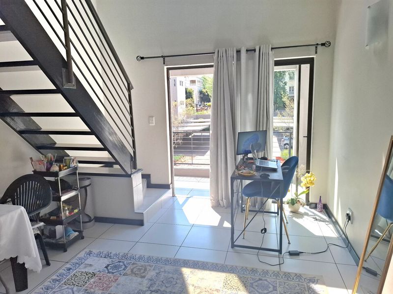A bright living area featuring tiled flooring, a modern metal staircase, and direct access to a balcony through a sliding glass door.