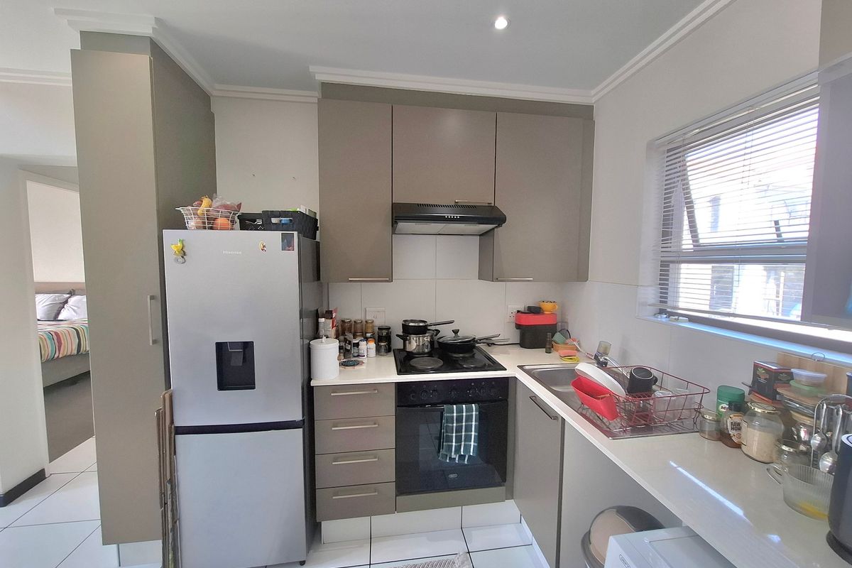 A compact, functional kitchen featuring modern cabinetry, built-in oven and hob, extractor fan, and tiled flooring with a view into the adjacent bedroom.