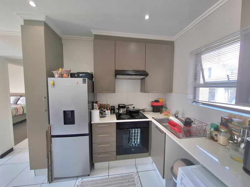 A compact, functional kitchen featuring modern cabinetry, built-in oven and hob, extractor fan, and tiled flooring with a view into the adjacent bedroom.