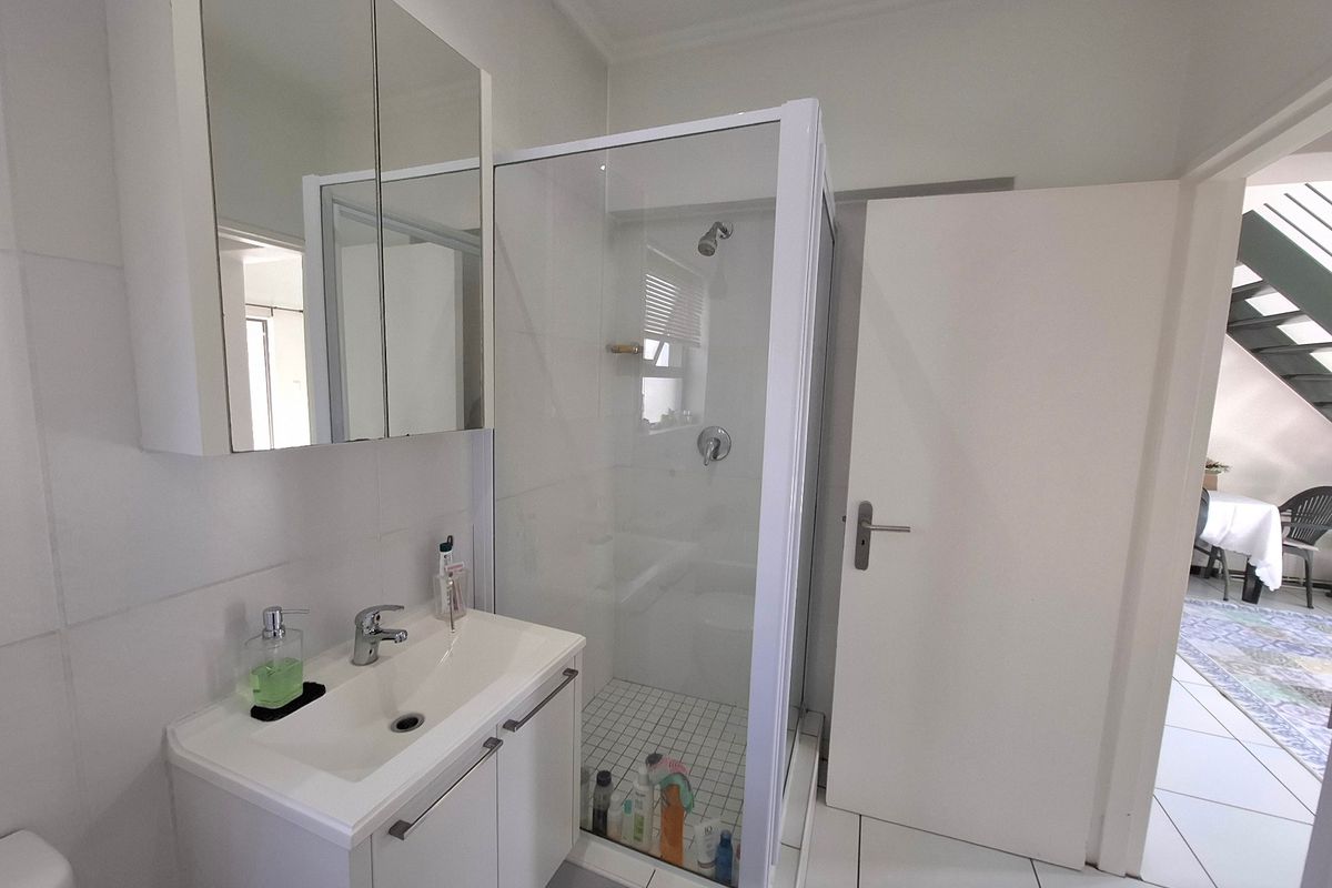 A clean, functional bathroom featuring a modern vanity with a mirrored cabinet and a separate glass-enclosed shower with white tiled flooring.