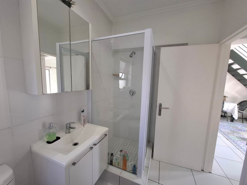 A clean, functional bathroom featuring a modern vanity with a mirrored cabinet and a separate glass-enclosed shower with white tiled flooring.