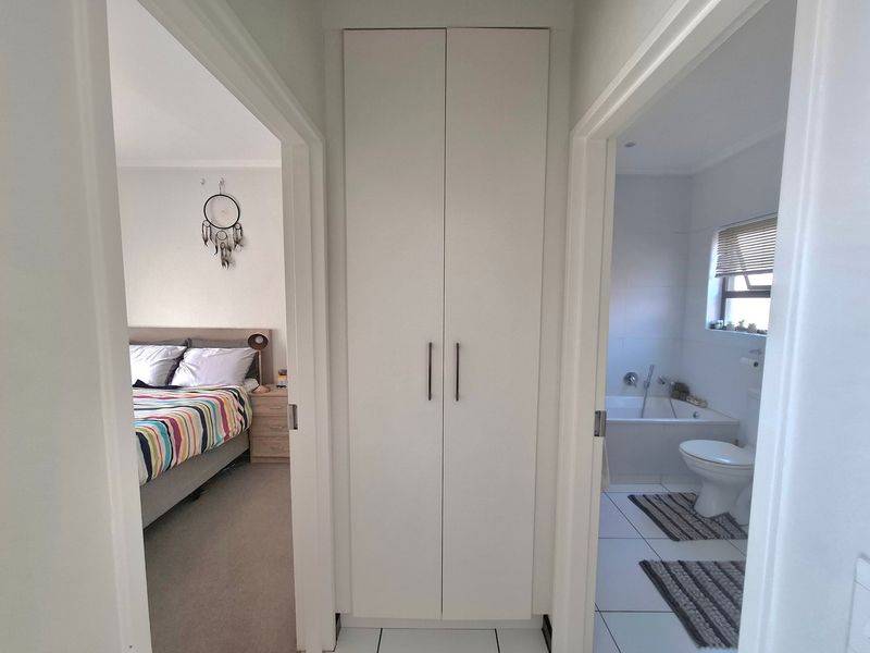 A clean hallway featuring a central built-in cupboard, providing access to an adjacent bedroom and bathroom.