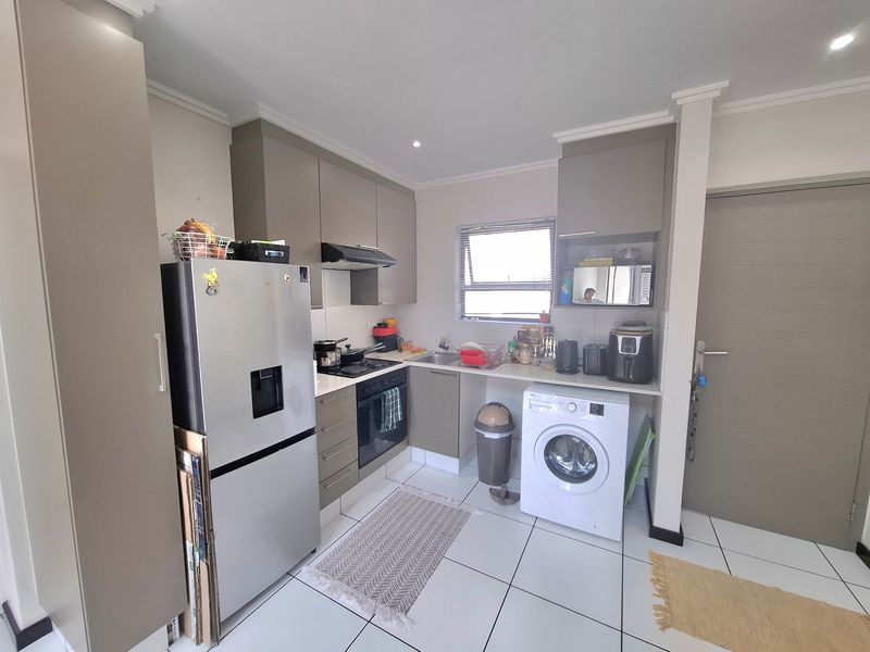 A functional kitchen featuring modern grey cabinetry, built-in oven and hob, stainless steel sink, and tiled flooring with space for a washing machine.