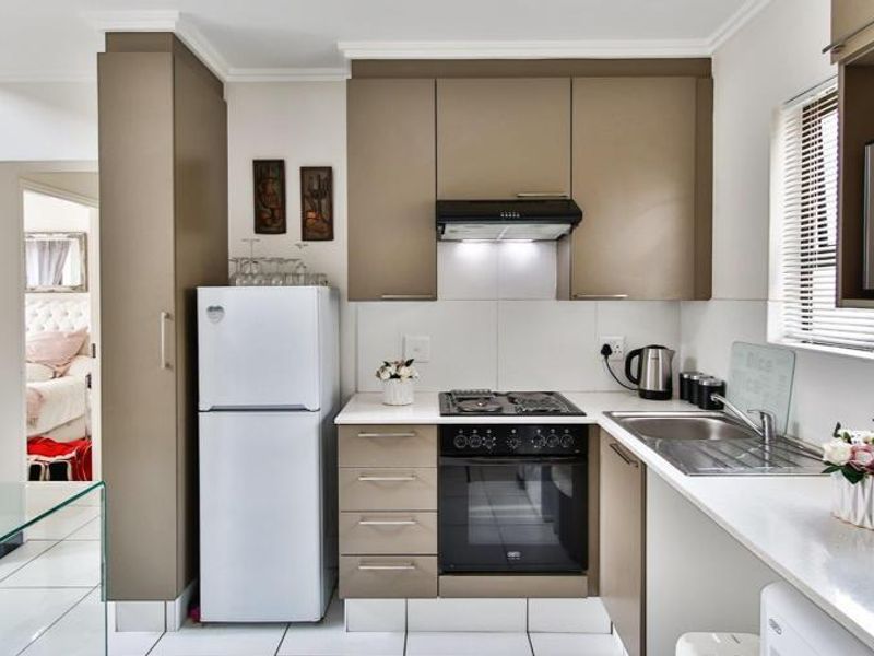 A compact, well-maintained kitchen featuring modern taupe cabinetry, a built-in gas hob, electric oven, extractor fan, and a stainless steel sink.