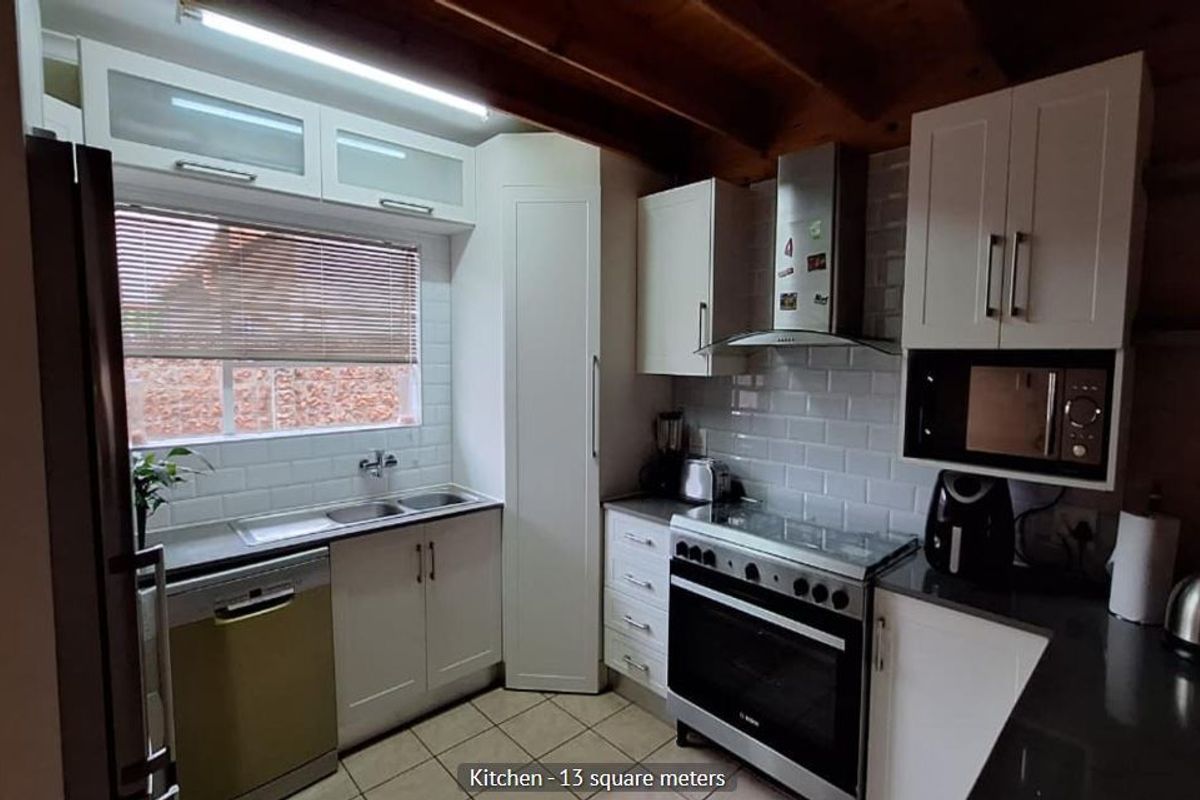 A well-appointed kitchen featuring white cabinetry, subway tile backsplash, stainless steel appliances, and exposed timber ceiling beams.