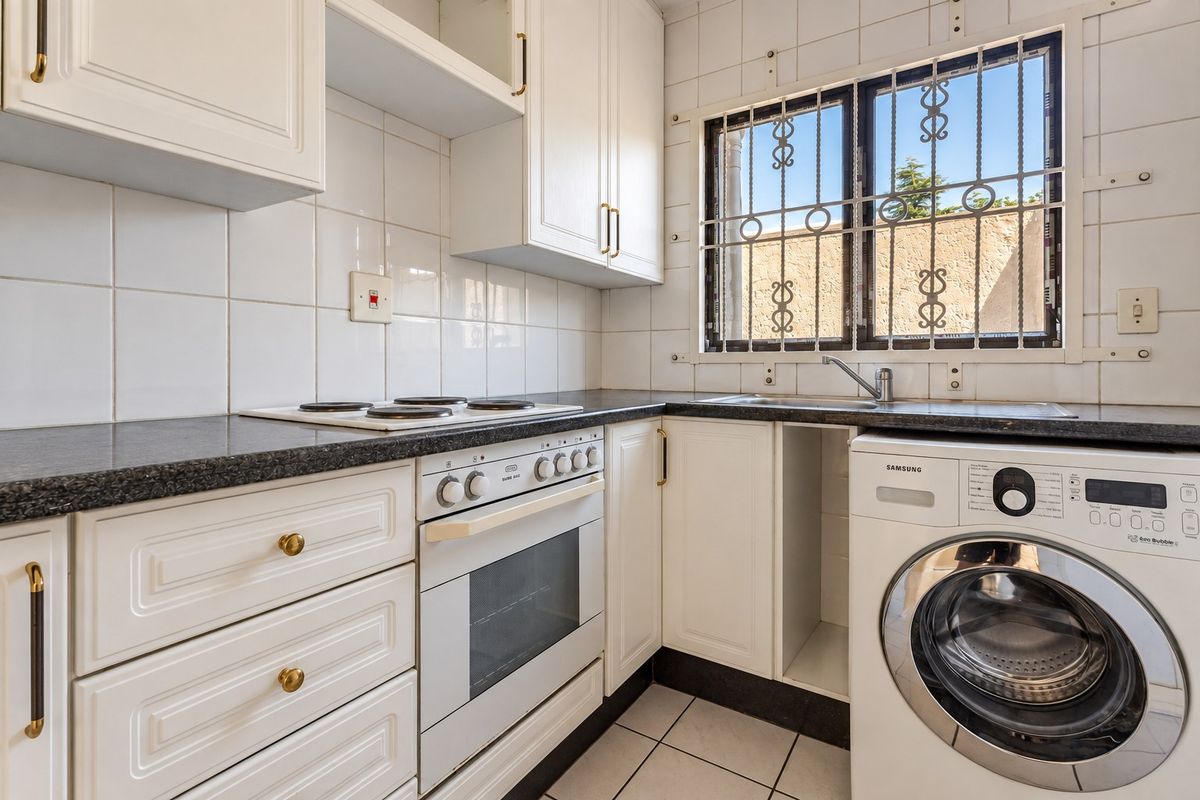 A functional kitchen featuring white cabinetry, granite countertops, a built-in oven and hob, and a tiled backsplash with a window security gate.